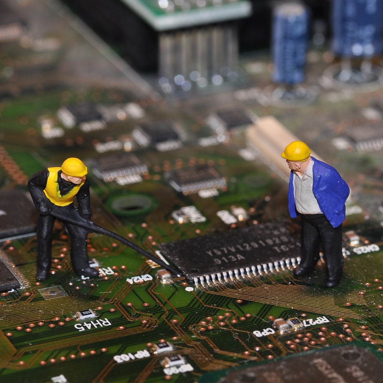 Two miniature figurines in hard hats working on a circuit board